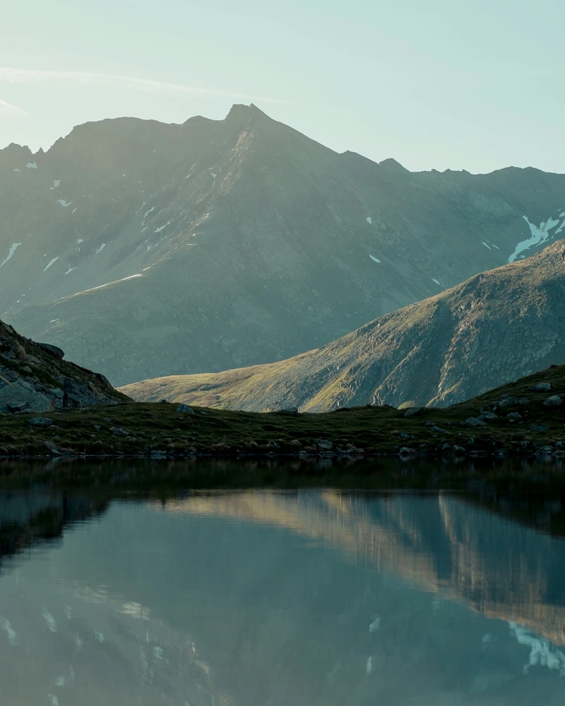 Lac de montagne calme reflétant un sommet, dans la lumière du matin.